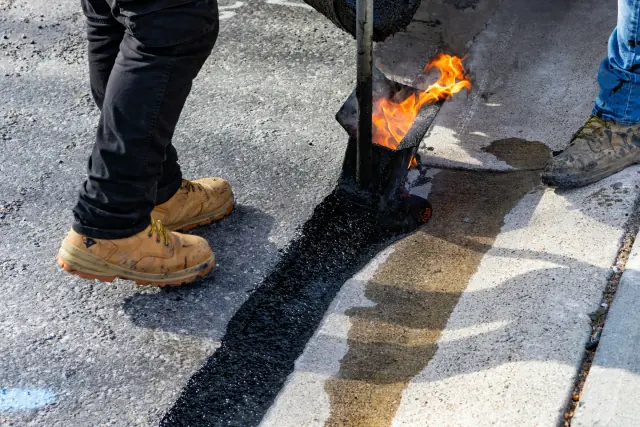 Workers applying hot asphalt sealant along a pavement joint